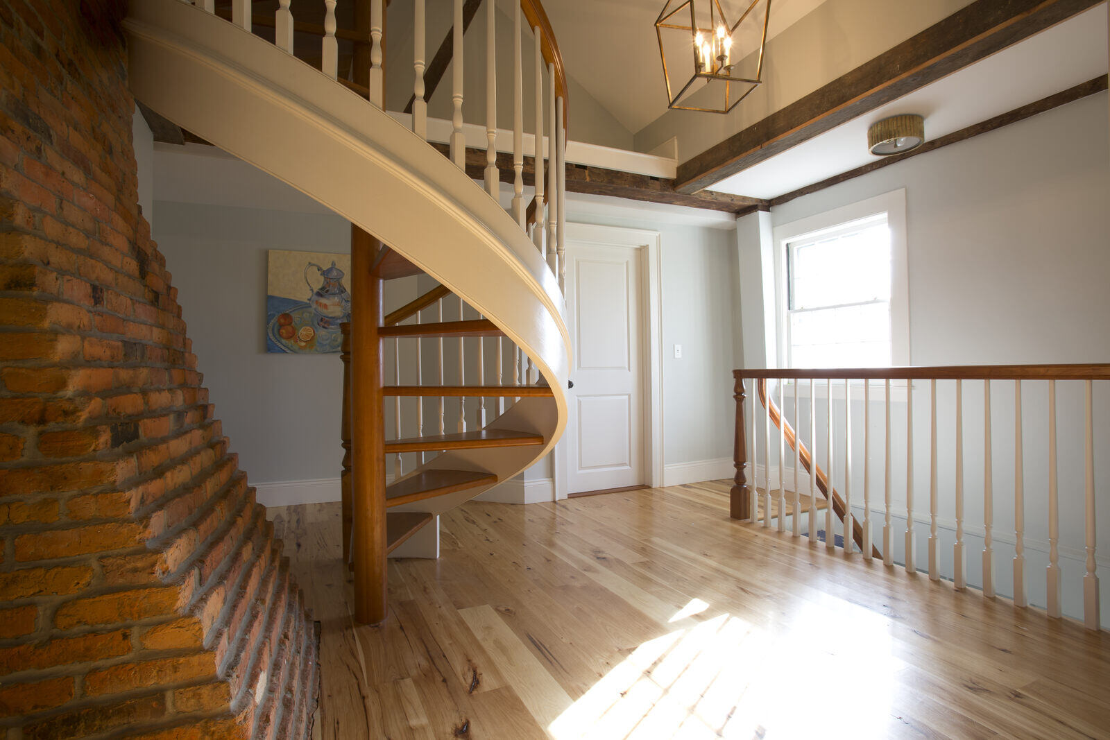 Interior view of a New Hampshire home remodeled by Oxland Builders, featuring a spiral staircase with exposed brick accents