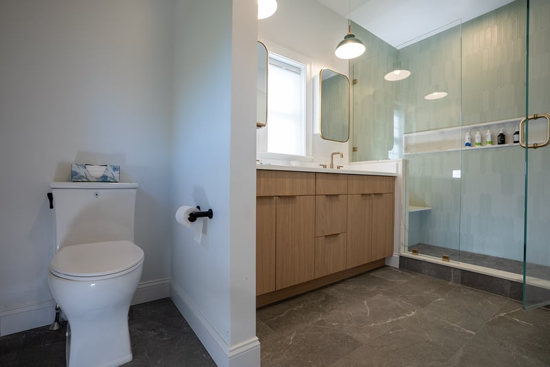 Contemporary Seacoast, NH bathroom featuring light wood vanity, dual mirrors, modern lighting, and a glass-enclosed shower with seafoam green tile