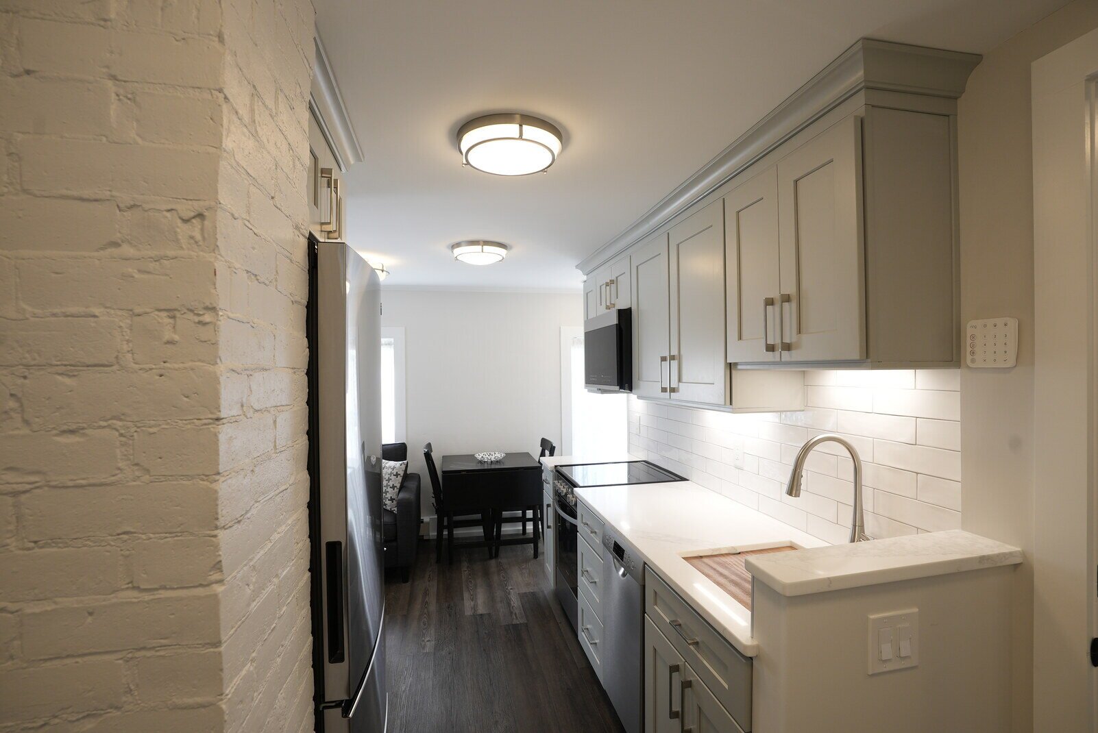 Galley-style kitchen with white cabinets and brick accents, remodeled by Oxland Builders in New Hampshire